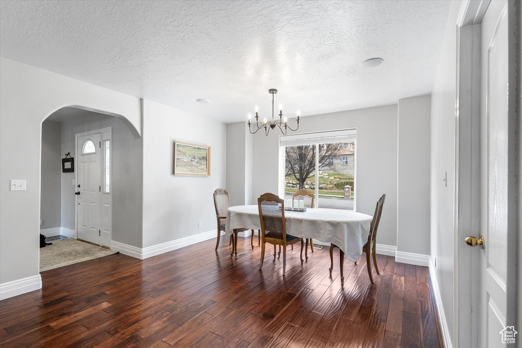 Dining space featuring wood finished floors, baseboards, a chandelier, a textured ceiling, and arched walkways