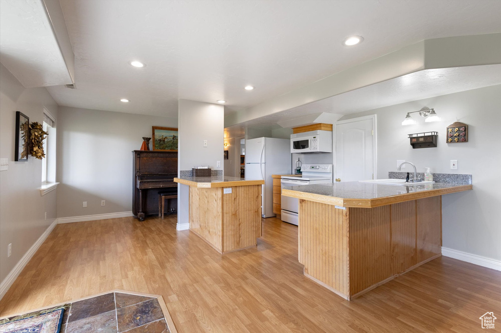 Kitchen with white appliances, a peninsula, light wood-style floors, baseboards, and a kitchen bar