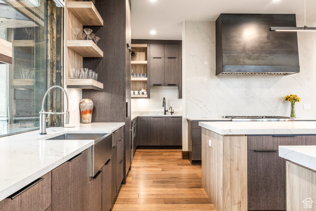 Kitchen with open shelves, modern cabinets, light wood-style floors, wall chimney range hood, and light stone counters