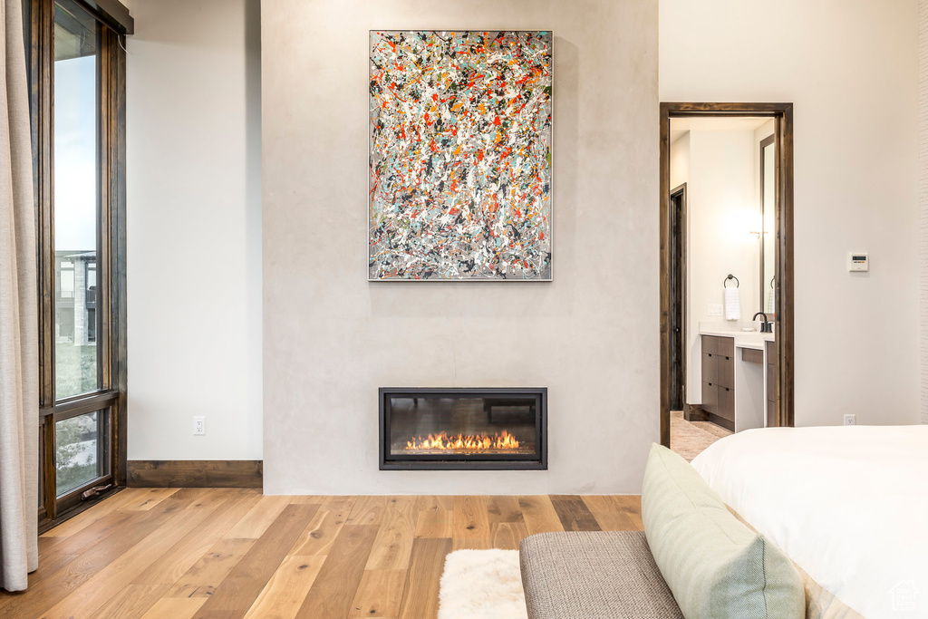 Bedroom with wood finished floors, a glass covered fireplace, baseboards, and connected bathroom