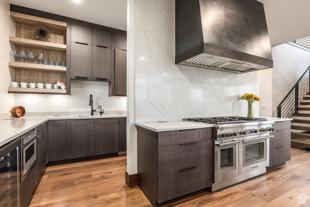 Kitchen featuring wall chimney range hood, double oven range, modern cabinets, beverage cooler, and dark brown cabinets