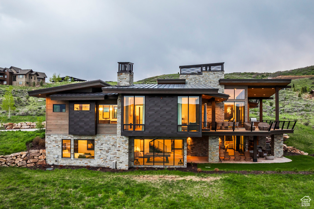 Back of house with a standing seam roof, a chimney, a yard, stone siding, and metal roof