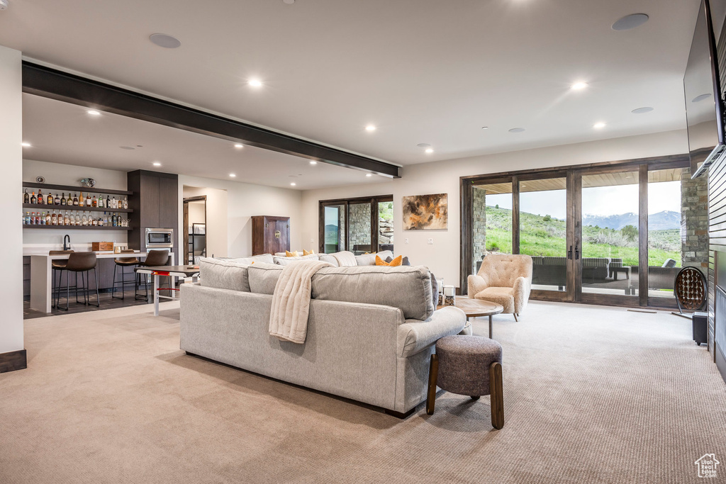 Living area featuring light colored carpet, bar with sink, beam ceiling, and recessed lighting