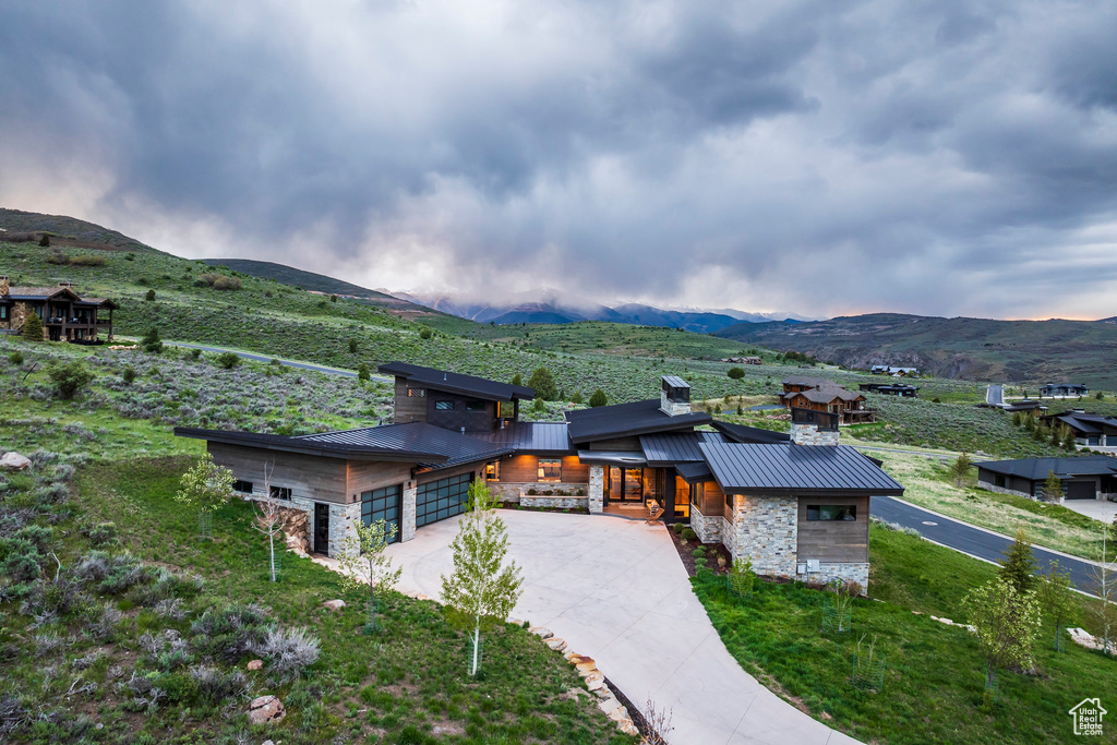 Contemporary house with stone siding, a mountain view, metal roof, and concrete driveway