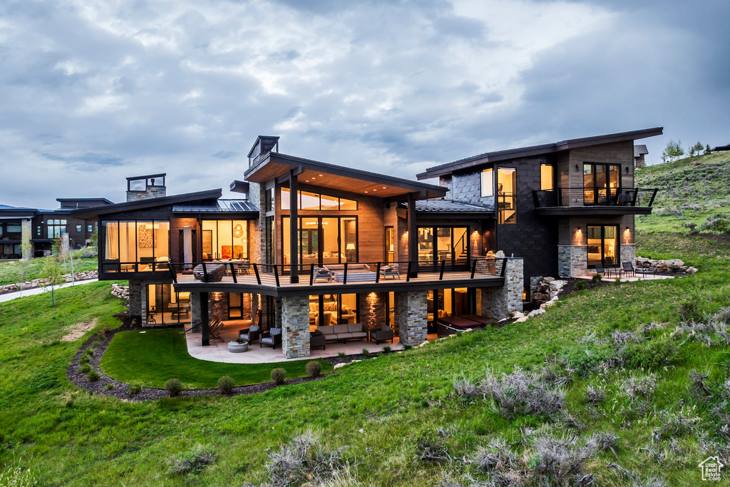 Rear view of property featuring a patio, an outdoor hangout area, stone siding, a standing seam roof, and a yard