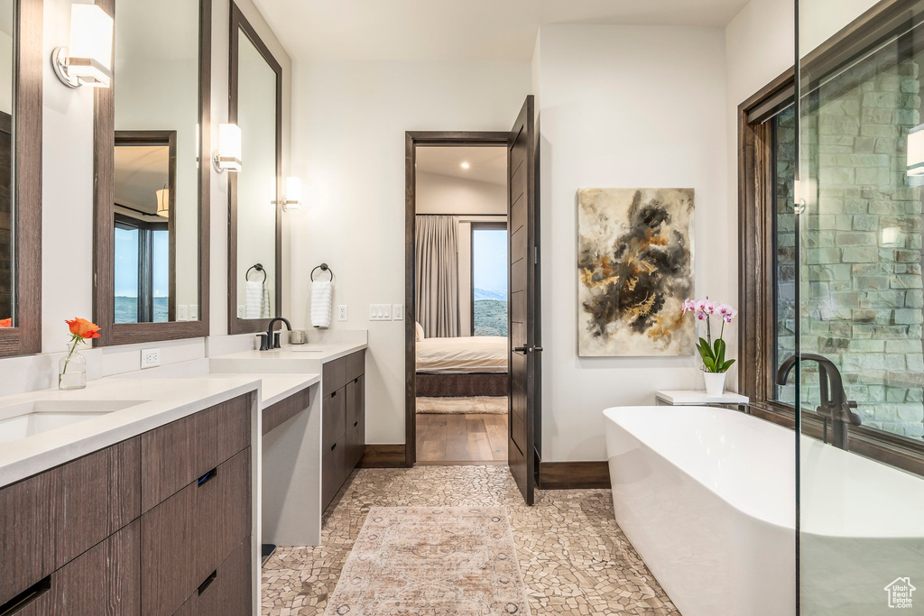 Ensuite bathroom featuring two vanities, a freestanding tub, baseboards, and a stall shower