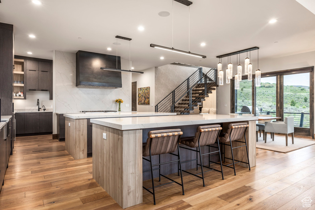 Kitchen with a large island, modern cabinets, light wood finished floors, wall chimney range hood, and recessed lighting