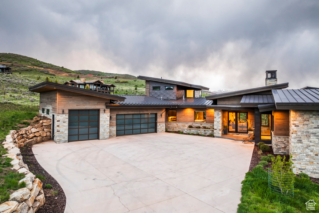 Modern home with a standing seam roof, a garage, stone siding, metal roof, and concrete driveway