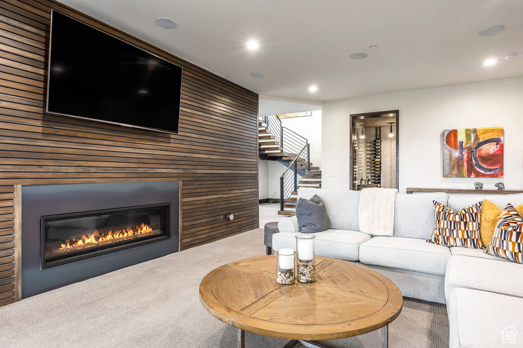 Living room featuring stairs, wood walls, a glass covered fireplace, carpet, and recessed lighting
