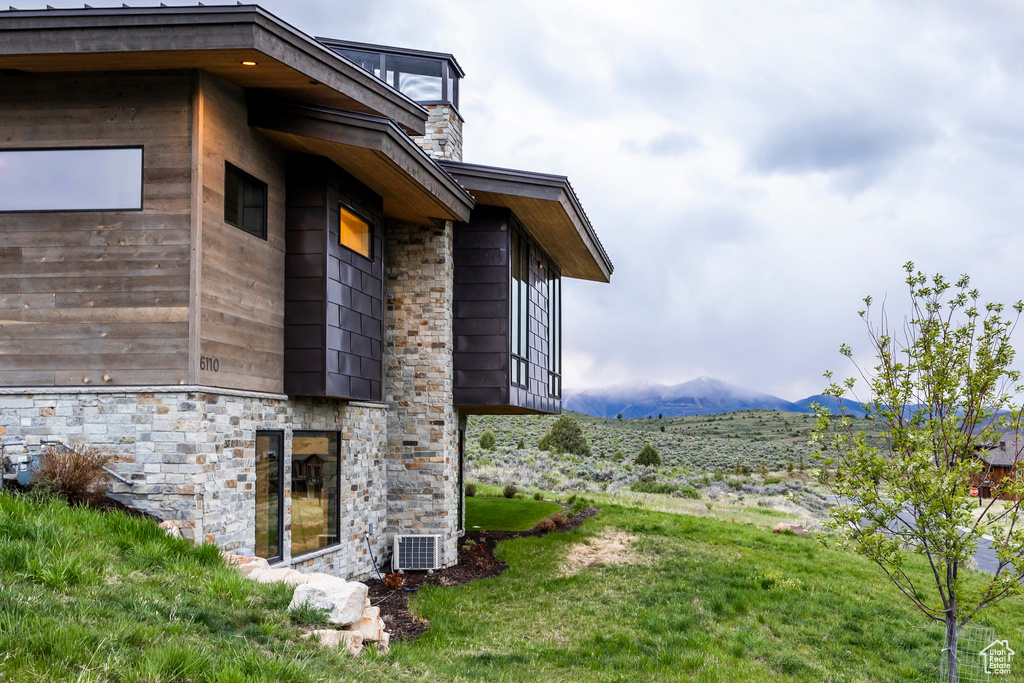 View of side of home featuring a mountain view, stone siding, a lawn, a balcony, and a chimney