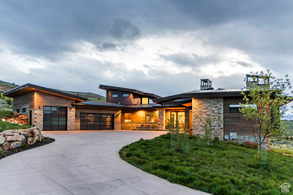 Contemporary house with a standing seam roof, a garage, stone siding, and metal roof
