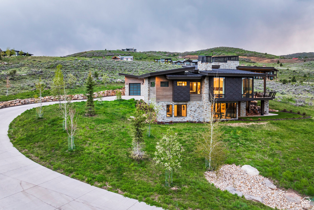 View of property exterior with stone siding, concrete driveway, an attached garage, and a lawn