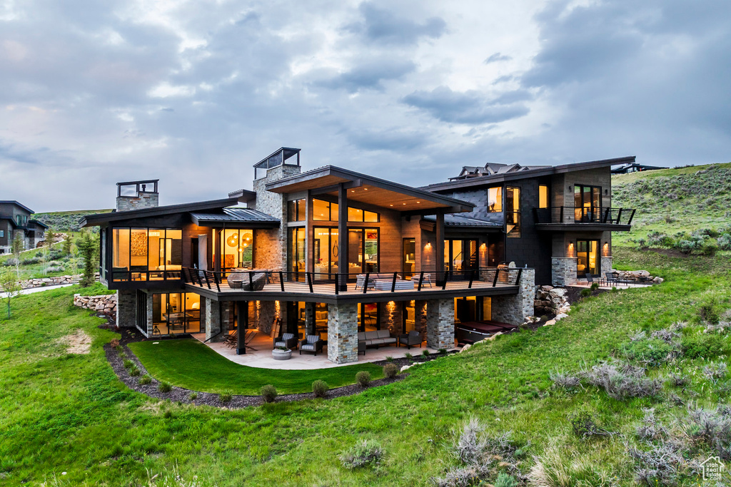 Rear view of property featuring a patio area, stone siding, a yard, a standing seam roof, and a chimney