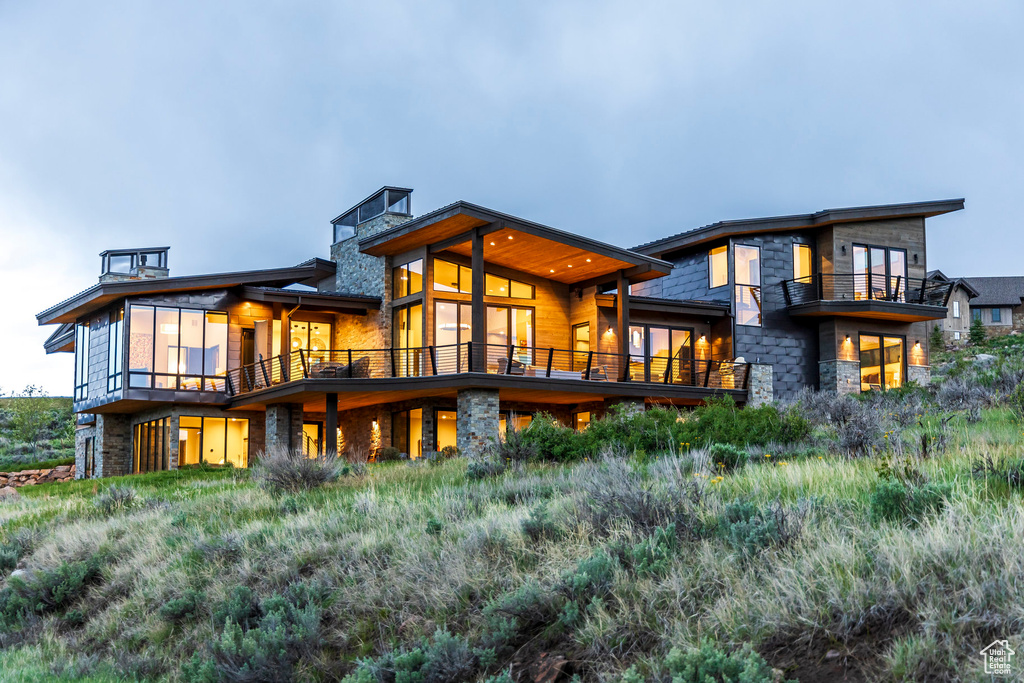 Rear view of property featuring a balcony and stone siding