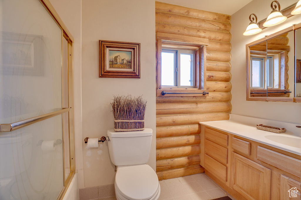 Full bath with log walls, vanity, toilet, and shower / bath combination with glass door