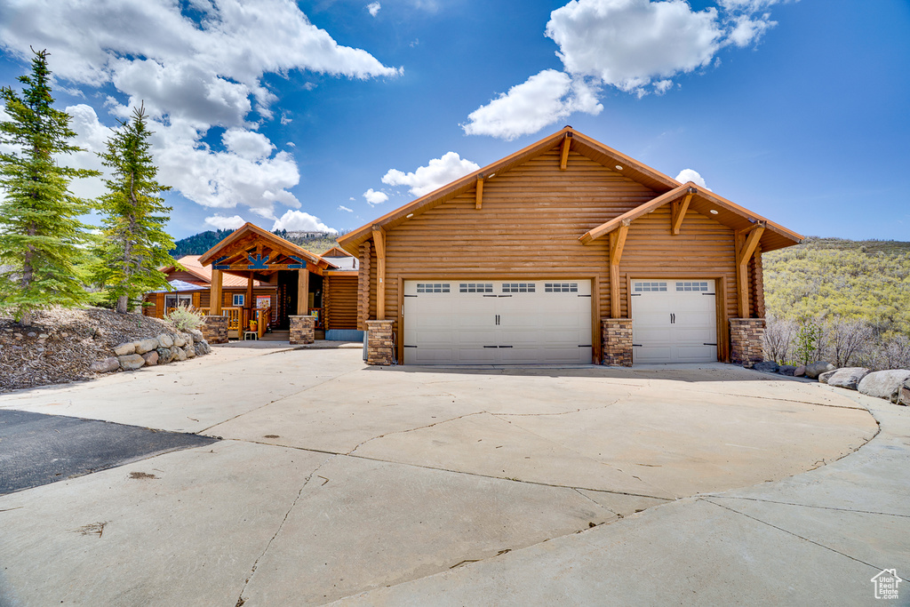 Log-style house with driveway, stone siding, and an attached garage