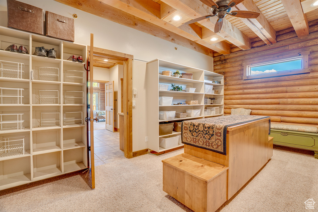 Interior space with wooden ceiling, light carpet, rustic walls, a ceiling fan, and beamed ceiling