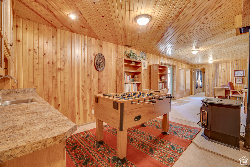 Recreation room featuring a sink, wooden walls, a wood stove, wood ceiling, and tile patterned flooring