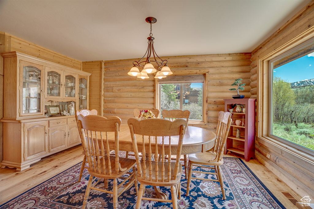 Dining area with log walls, light wood finished floors, plenty of natural light, and a chandelier
