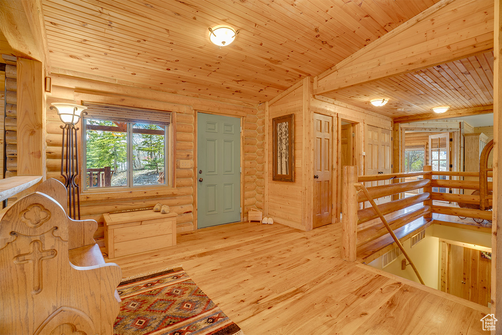 Unfurnished room featuring an upstairs landing, healthy amount of natural light, log walls, wood ceiling, and wood finished floors