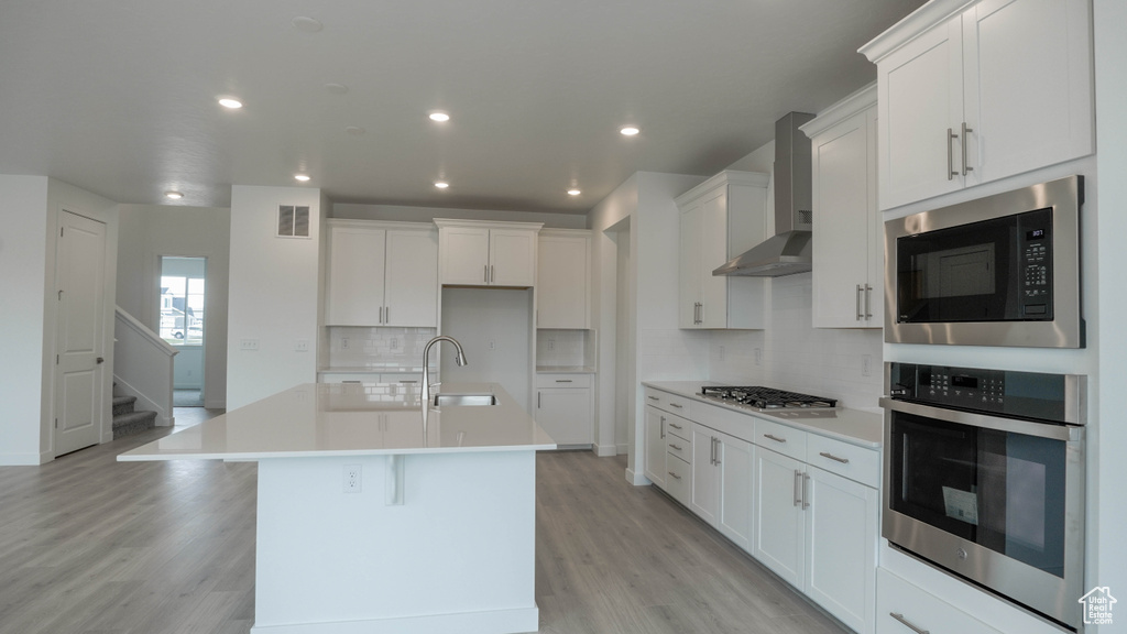 Kitchen with stainless steel appliances, wall chimney range hood, a sink, a kitchen island with sink, and decorative backsplash