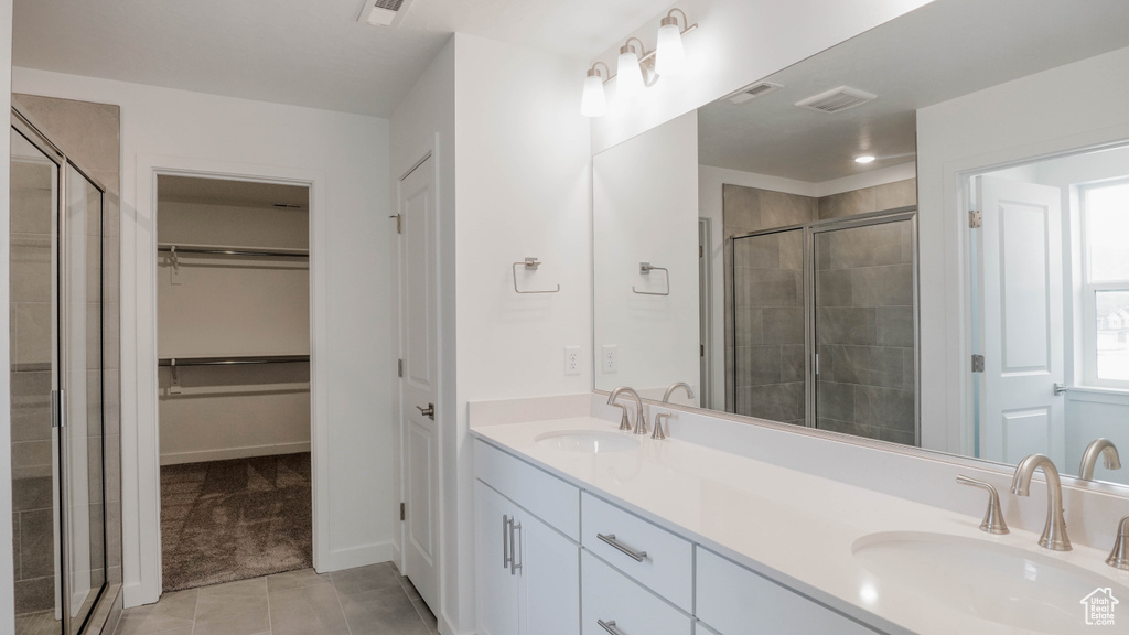 Full bathroom featuring double vanity, a shower stall, a spacious closet, and tile patterned flooring