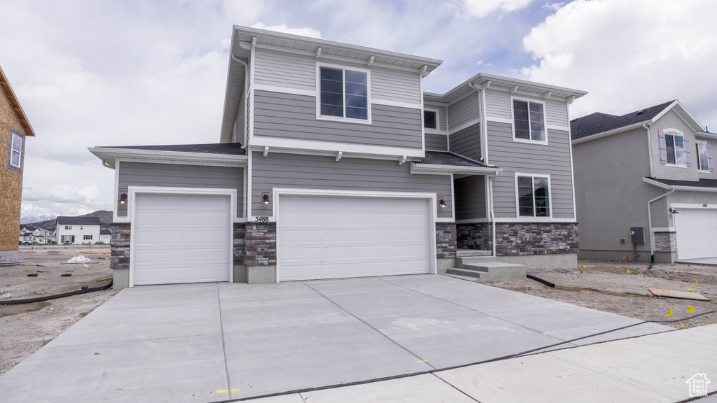 View of front of property featuring stone siding, an attached garage, and driveway
