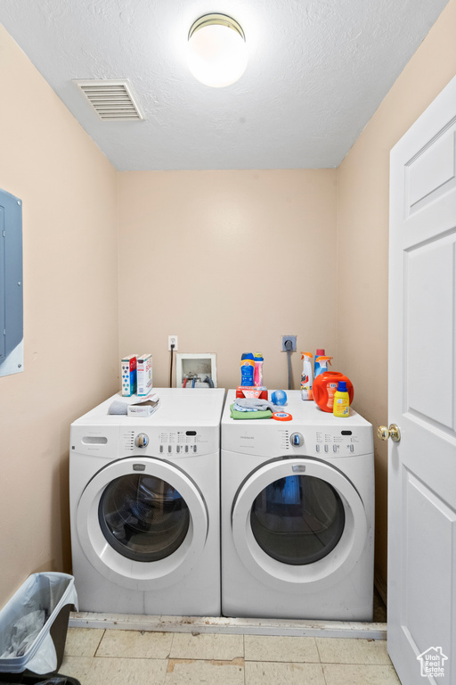 Laundry room with washer and clothes dryer, electric panel, and a textured ceiling