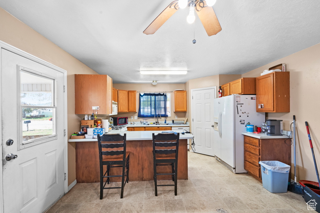 Kitchen featuring white appliances, a peninsula, light countertops, a sink, and a kitchen bar