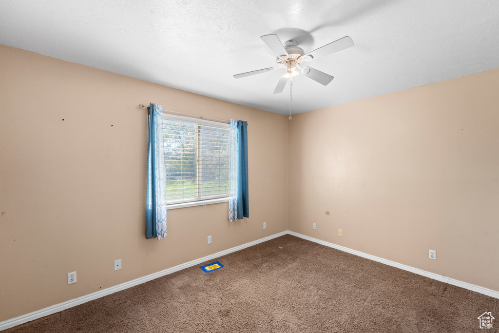 Carpeted spare room featuring ceiling fan and baseboards