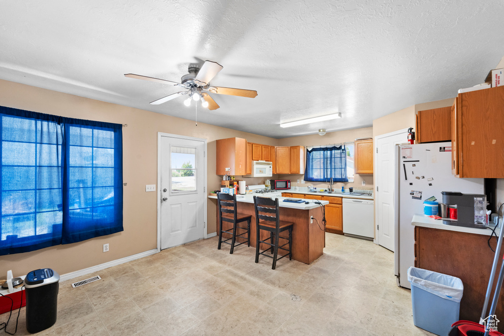 Kitchen with white appliances, a peninsula, a breakfast bar, a ceiling fan, and light countertops