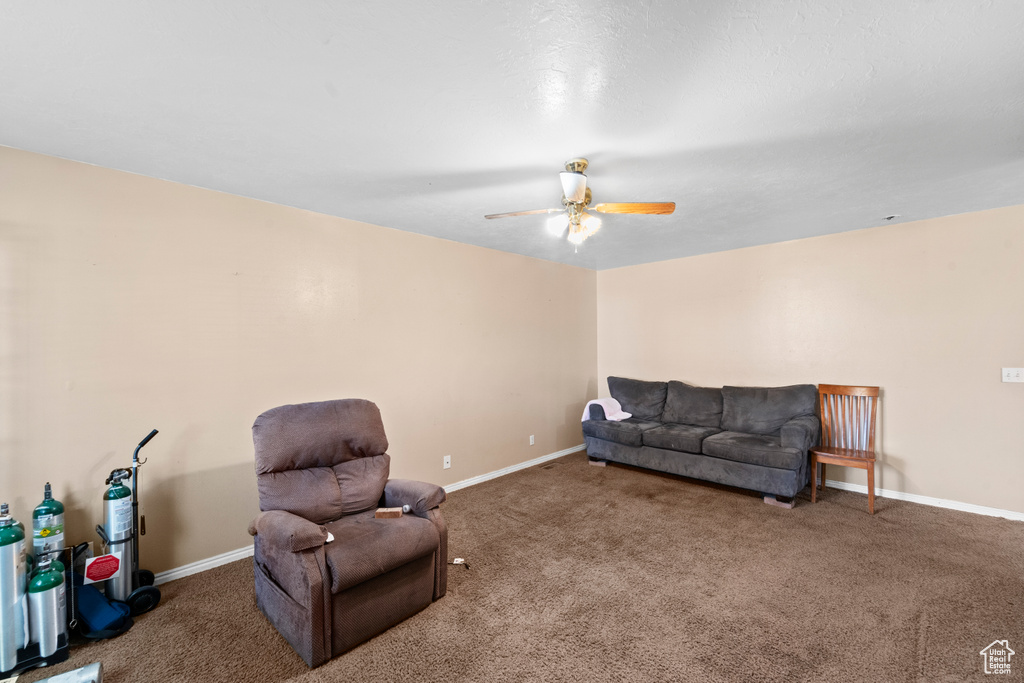 Carpeted living room featuring ceiling fan and baseboards