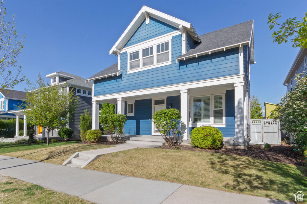 View of front facade with a porch, a shingled roof, fence, and a front yard