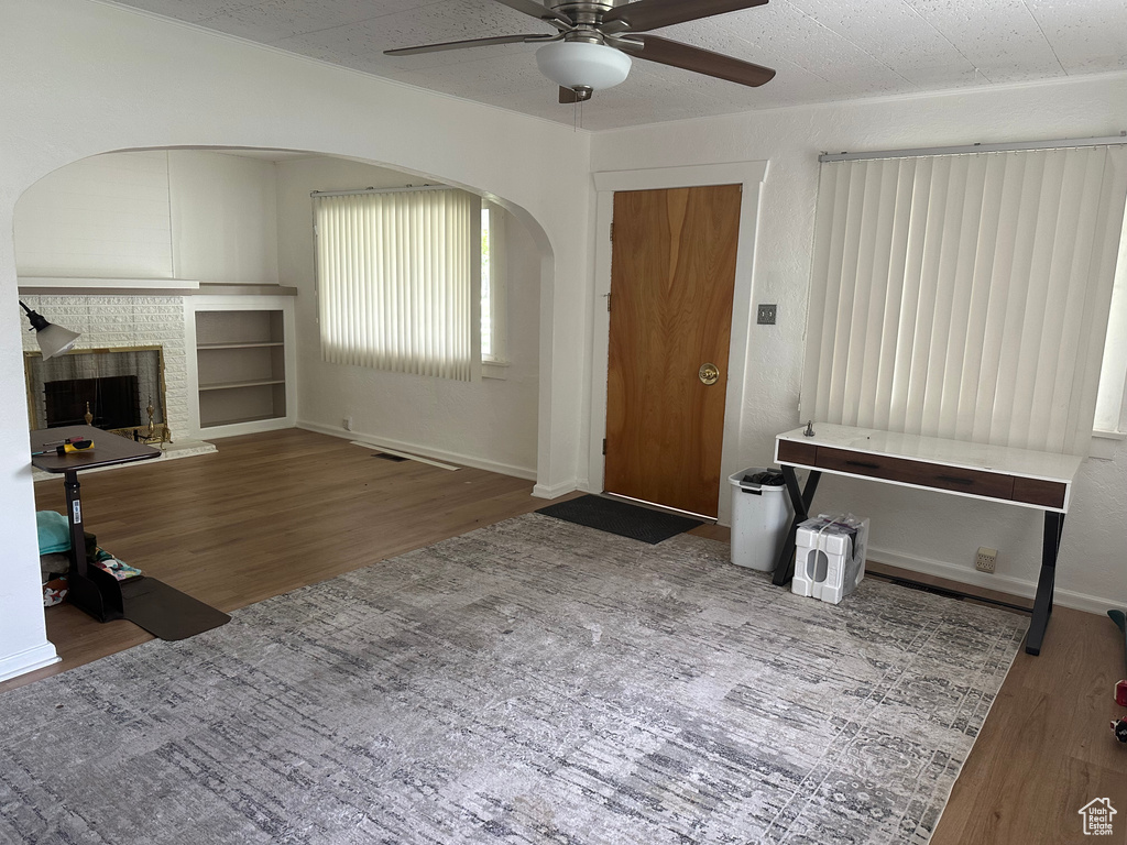 Unfurnished living room with a ceiling fan, wood finished floors, a brick fireplace, and arched walkways