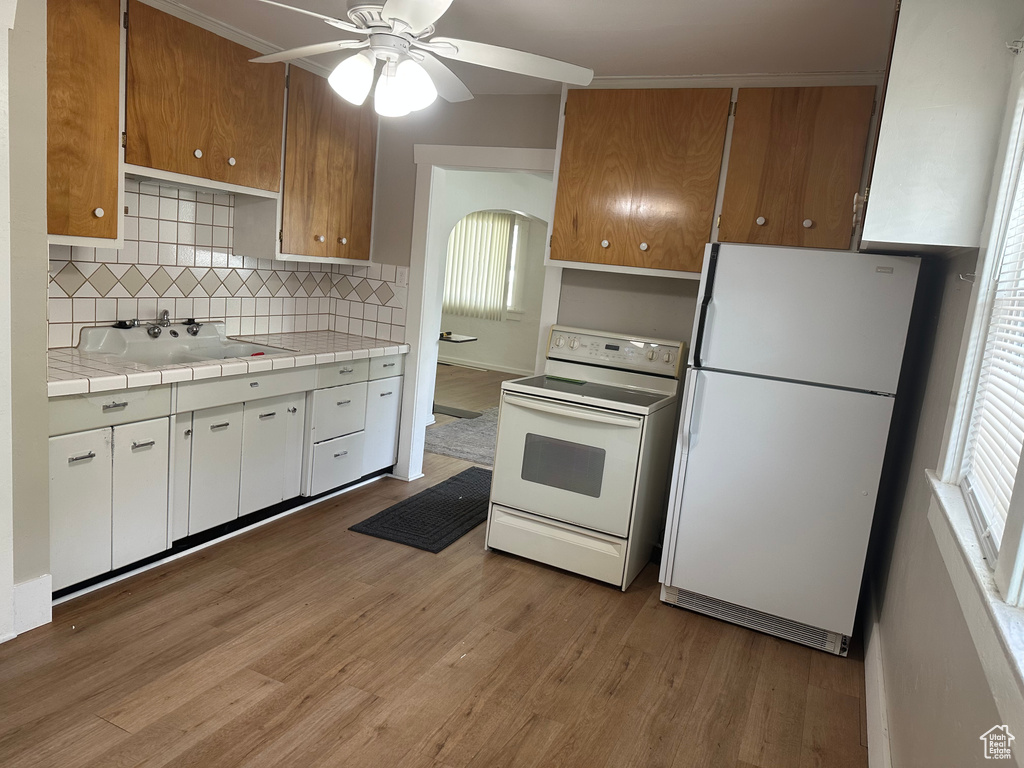 Kitchen featuring white appliances, a sink, light wood finished floors, backsplash, and a ceiling fan