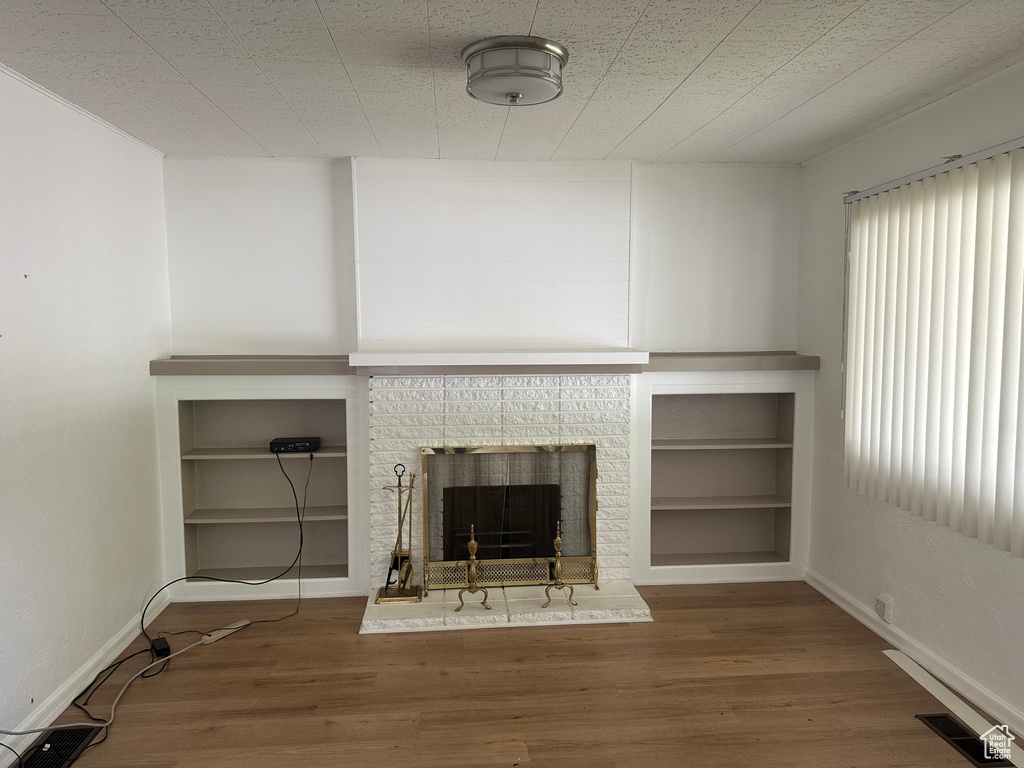 Unfurnished living room with wood finished floors, a fireplace, built in shelves, and baseboards