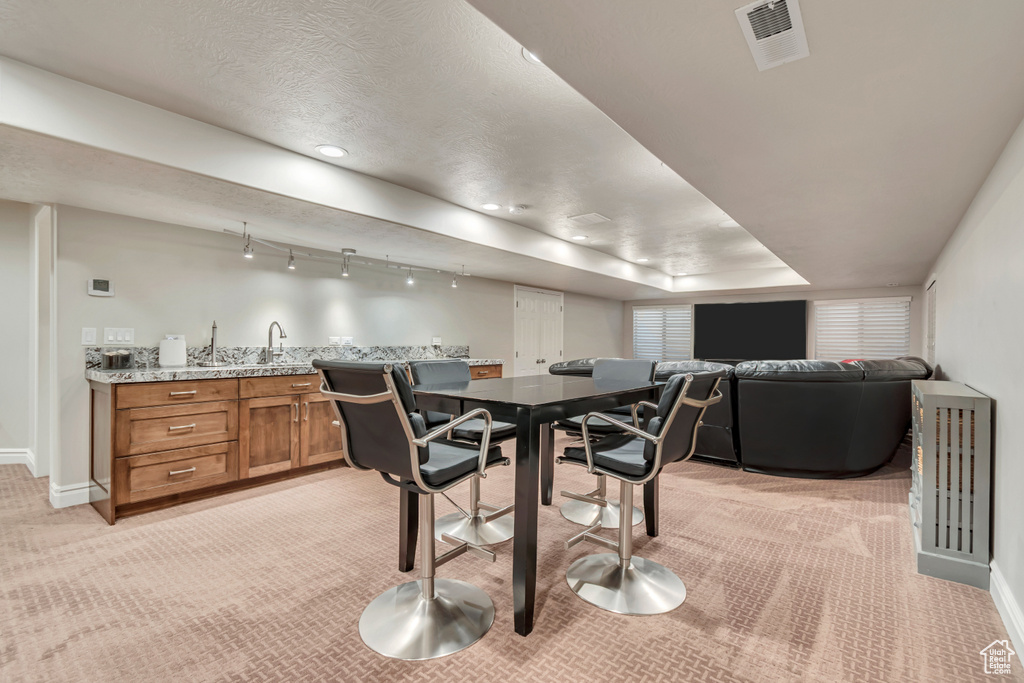 Dining room featuring light colored carpet, bar with sink, and baseboards