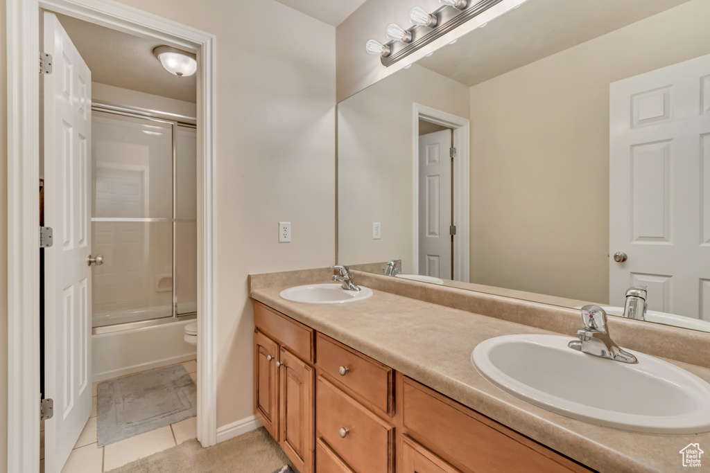 Full bathroom with tile patterned flooring, double vanity, toilet, and enclosed tub / shower combo