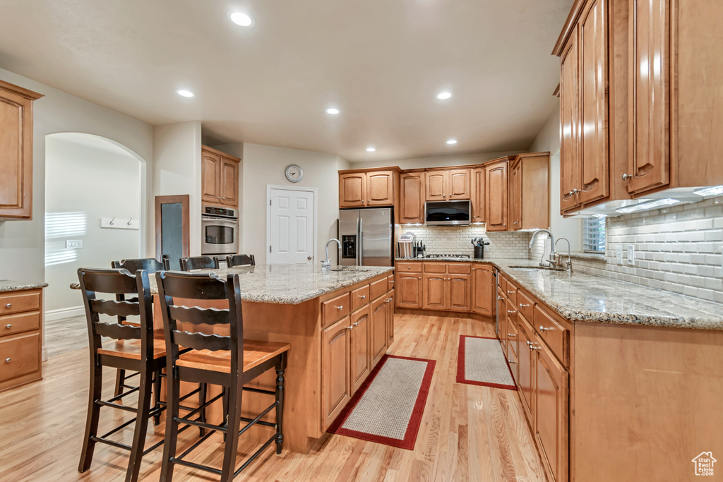Kitchen featuring stainless steel appliances, a sink, light wood-style floors, tasteful backsplash, and a breakfast bar area