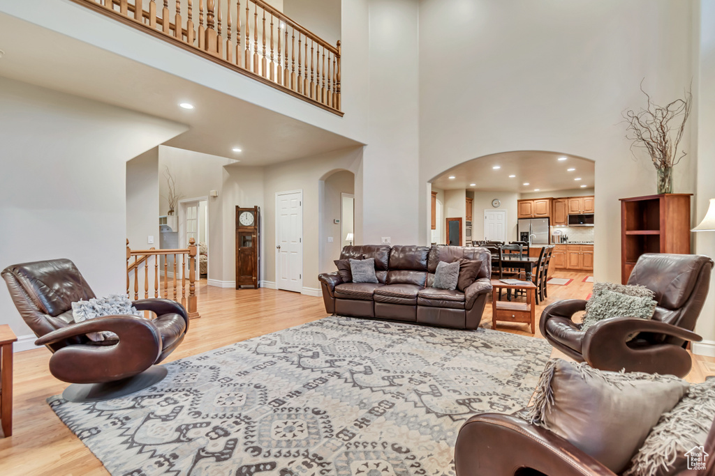 Living room featuring arched walkways, light wood-type flooring, a towering ceiling, recessed lighting, and baseboards