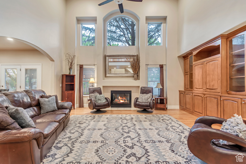 Living area with a high ceiling, a ceiling fan, arched walkways, a glass covered fireplace, and light wood-style floors