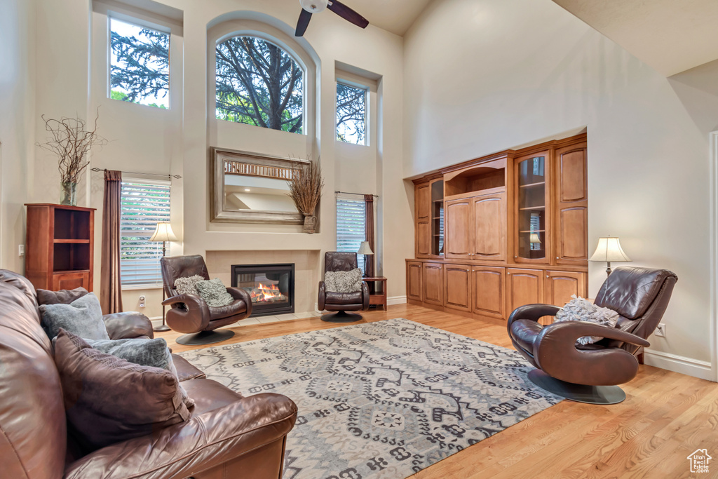 Living area featuring a high ceiling, light wood finished floors, ceiling fan, a fireplace with flush hearth, and baseboards