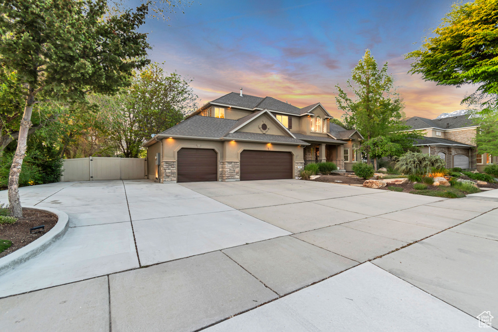 View of front of home featuring a gate, an attached garage, driveway, stone siding, and stucco siding