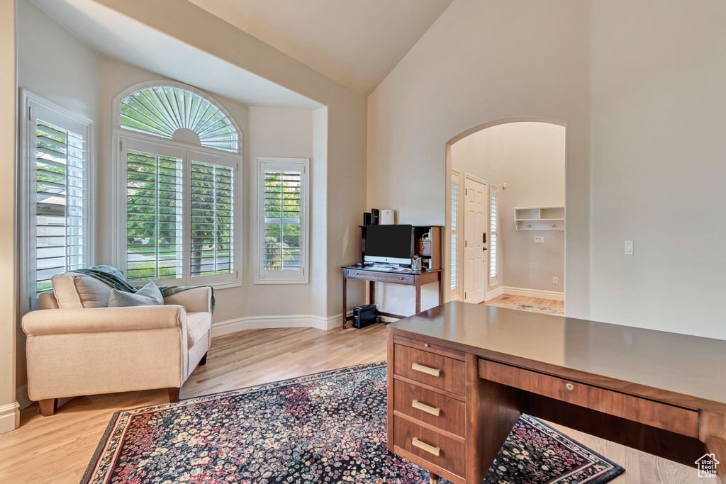 Office space featuring arched walkways, light wood finished floors, baseboards, and high vaulted ceiling