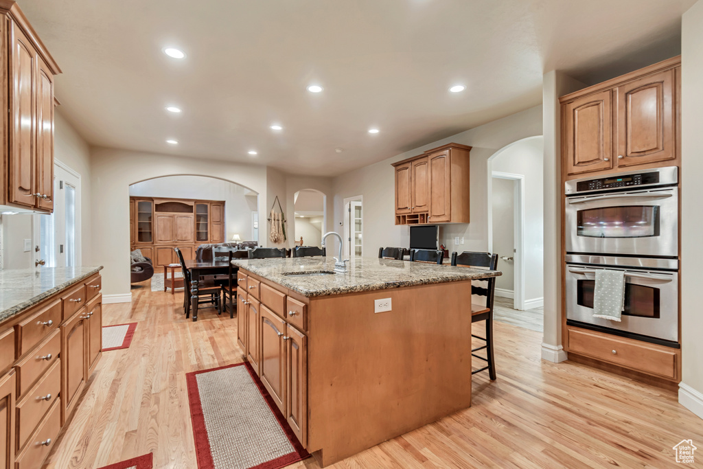 Kitchen featuring arched walkways, stainless steel double oven, a sink, an island with sink, and a breakfast bar area