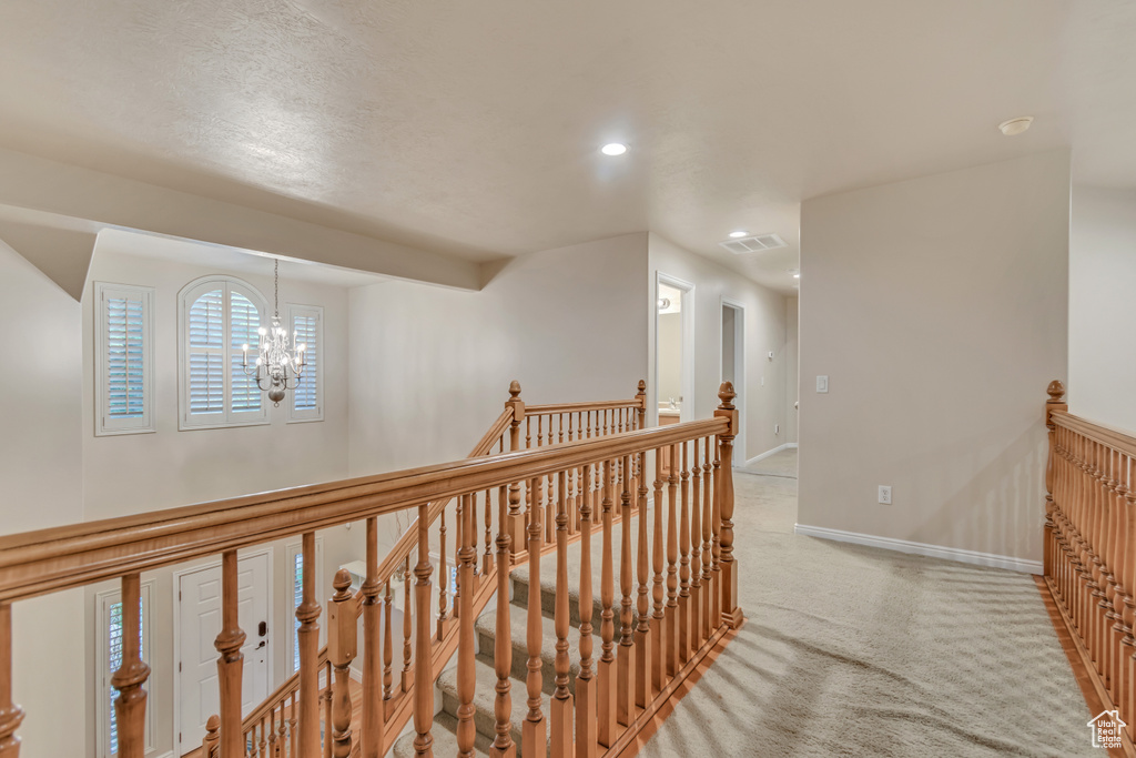 Corridor with an upstairs landing, light colored carpet, baseboards, recessed lighting, and a chandelier