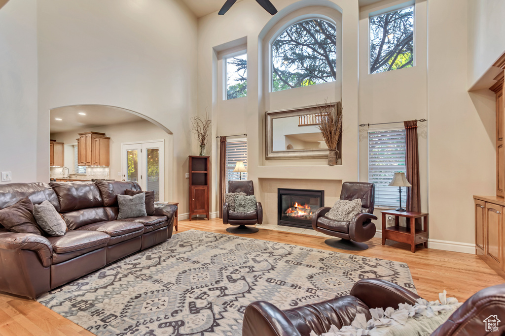Living room featuring a towering ceiling, a fireplace with flush hearth, light wood-style flooring, plenty of natural light, and a ceiling fan