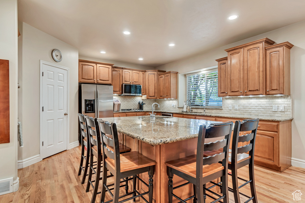 Kitchen with stainless steel appliances, a sink, light wood-style floors, a breakfast bar area, and recessed lighting