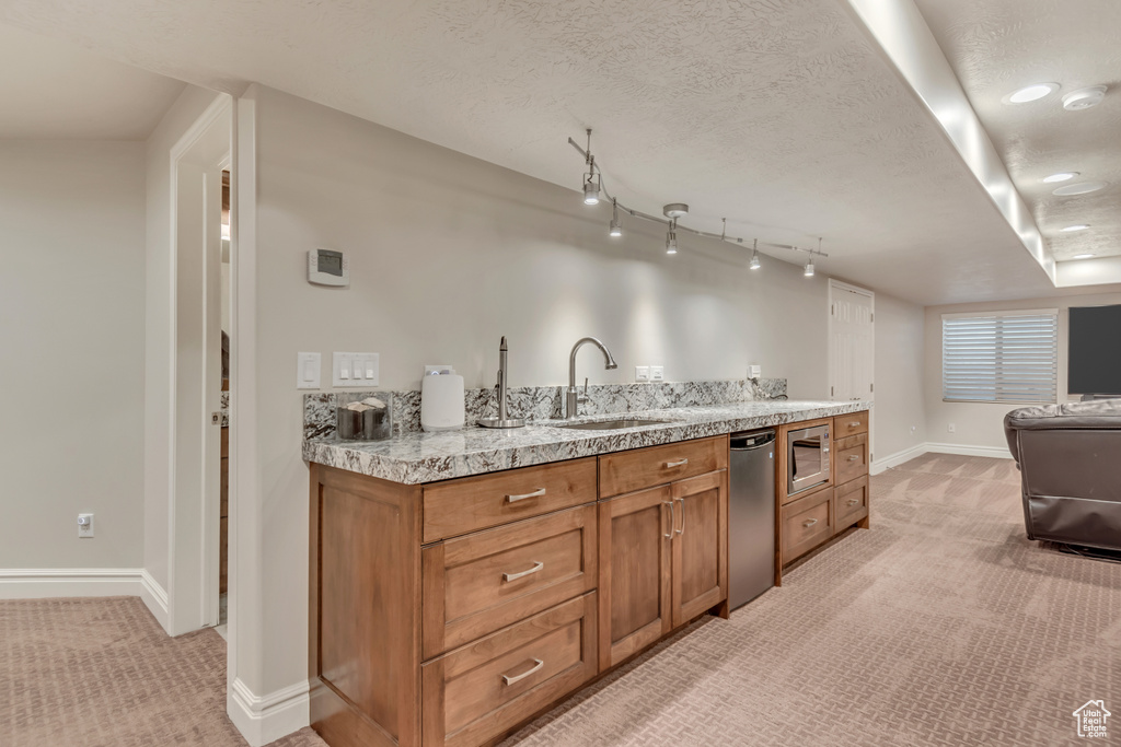 Kitchen with a sink, light colored carpet, appliances with stainless steel finishes, brown cabinetry, and a textured ceiling