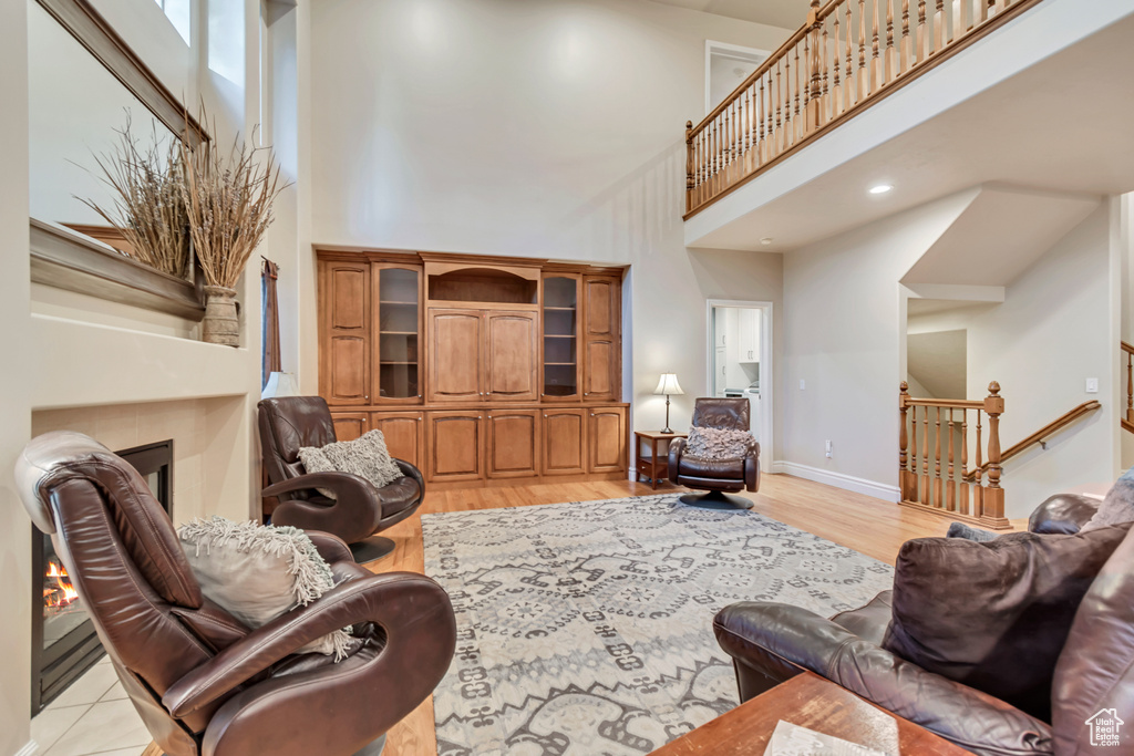 Living room with a tiled fireplace, a towering ceiling, light wood finished floors, baseboards, and stairway